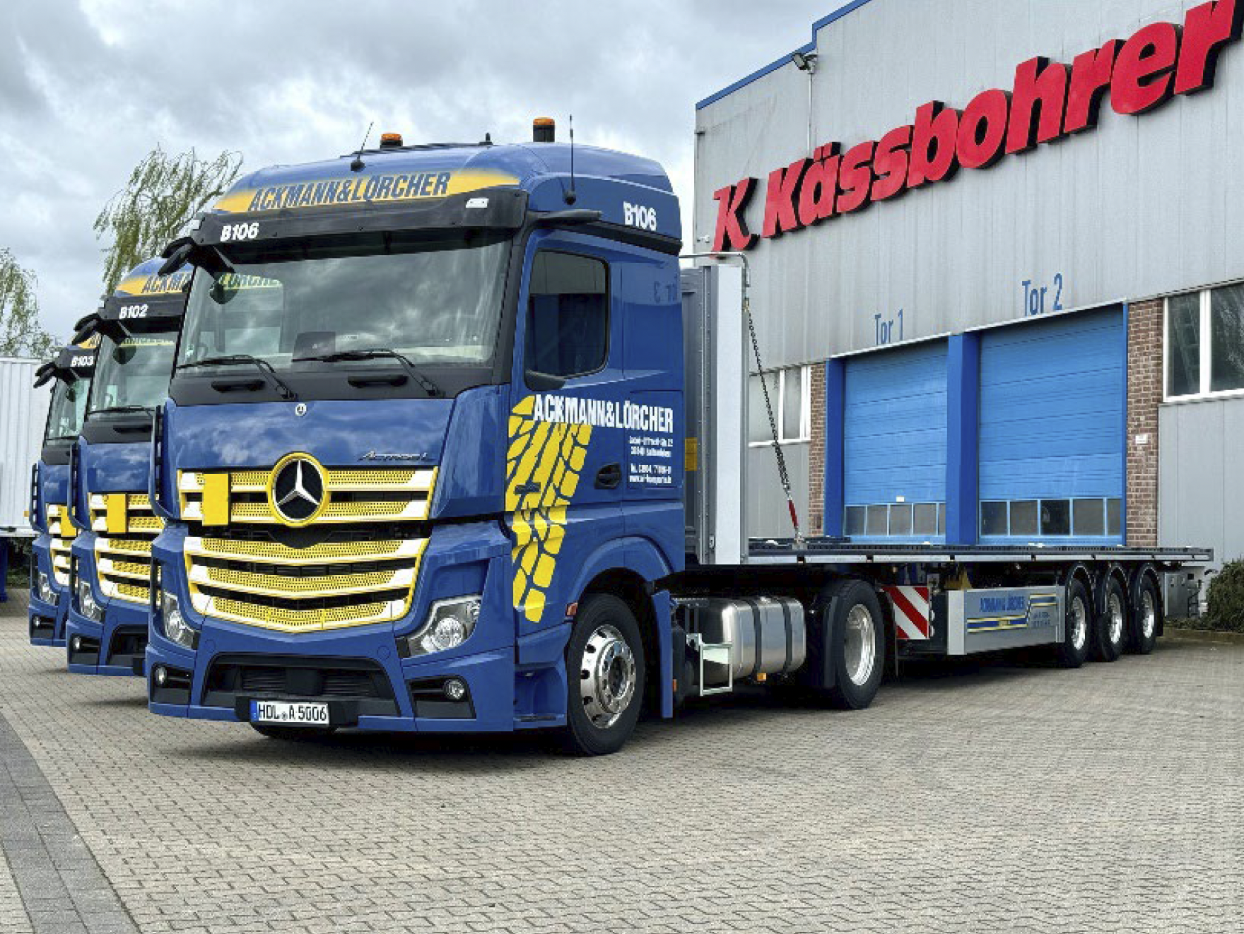 Drei Transport-LKW von Ackmann & Lörcher vor Industriehalle